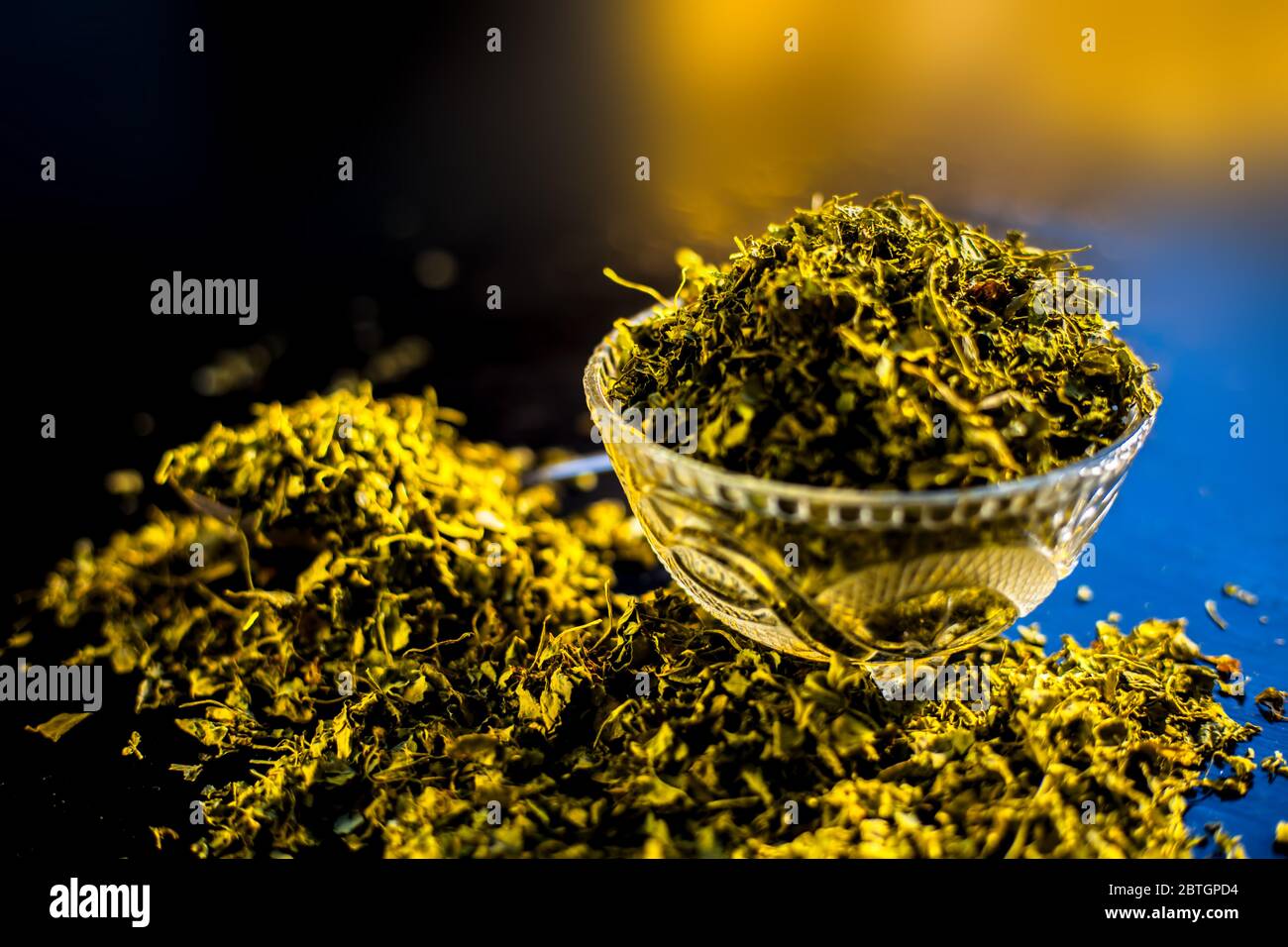 Close up short of popular Indian Spice Kasuri Methi (Dried Fenugreek Leaves) in a bowl and some on a spoon on a black colored glossy surface. Stock Photo