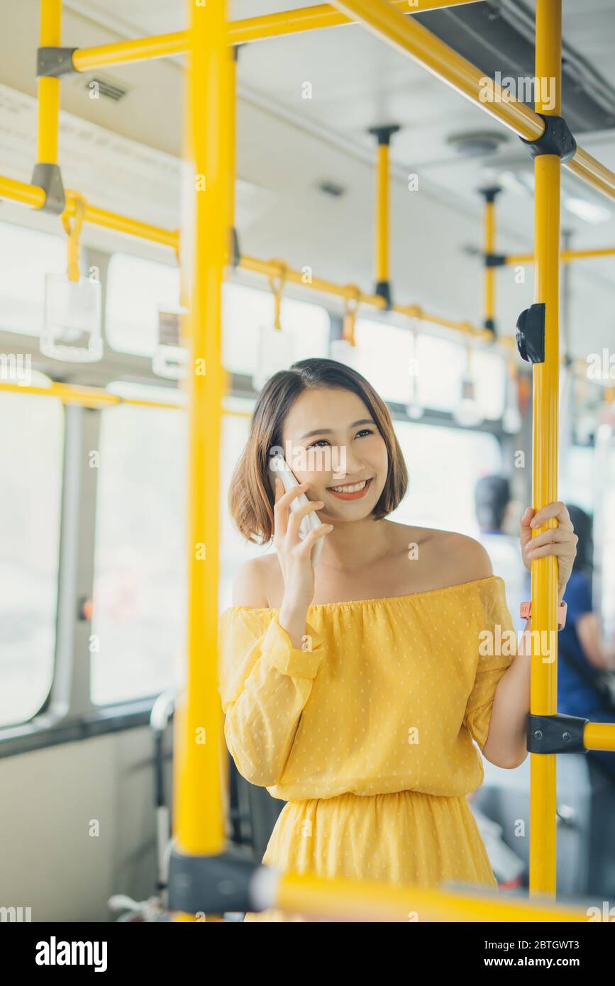 Portrait of young Asian woman using phone and standing on the bus/ public transportation. Stock Photo