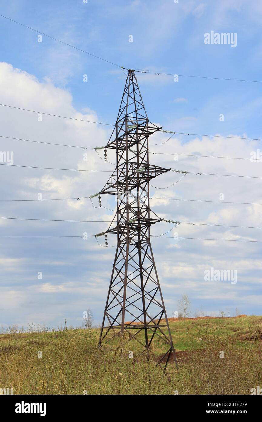 Iron pylon of a high voltage power line stands in a field against a blue sky. Stock Photo