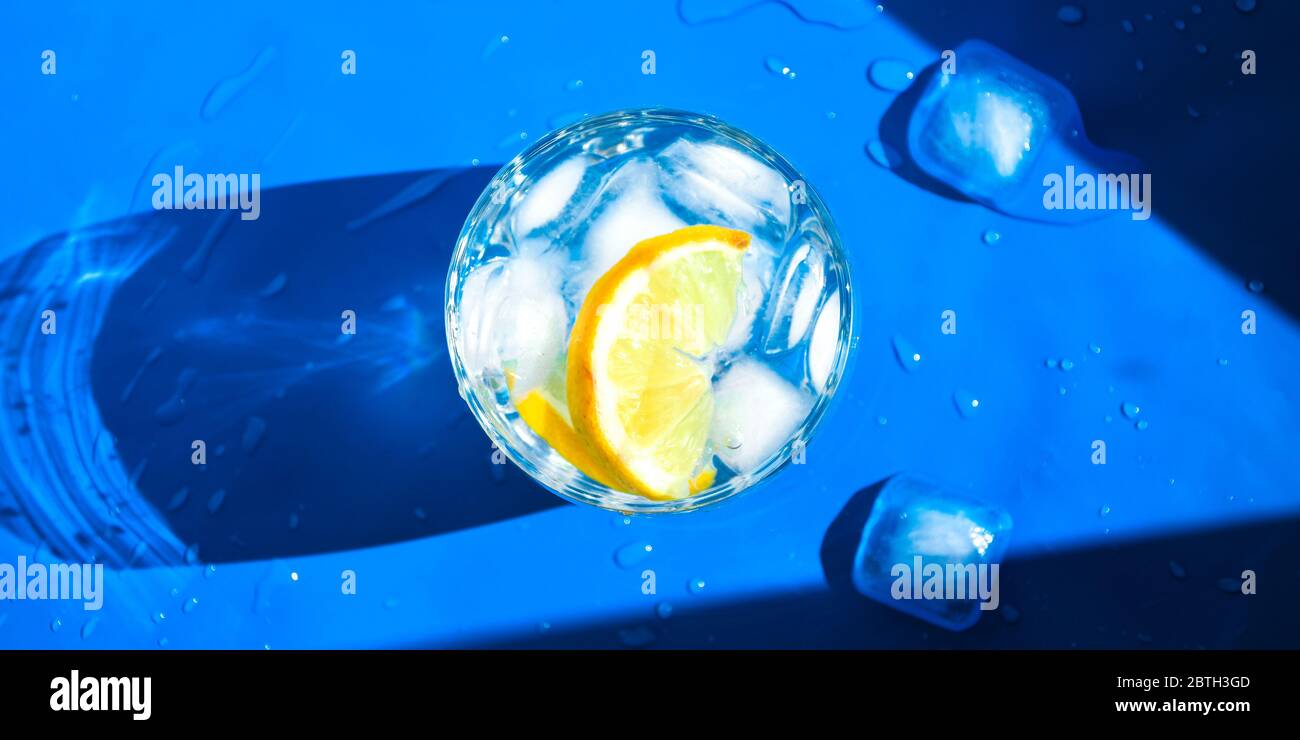 A glass of refreshing water with ice and lemon on a blue background. Heat concept, fresh. Natural light. Flat lay, top view, copy space Stock Photo
