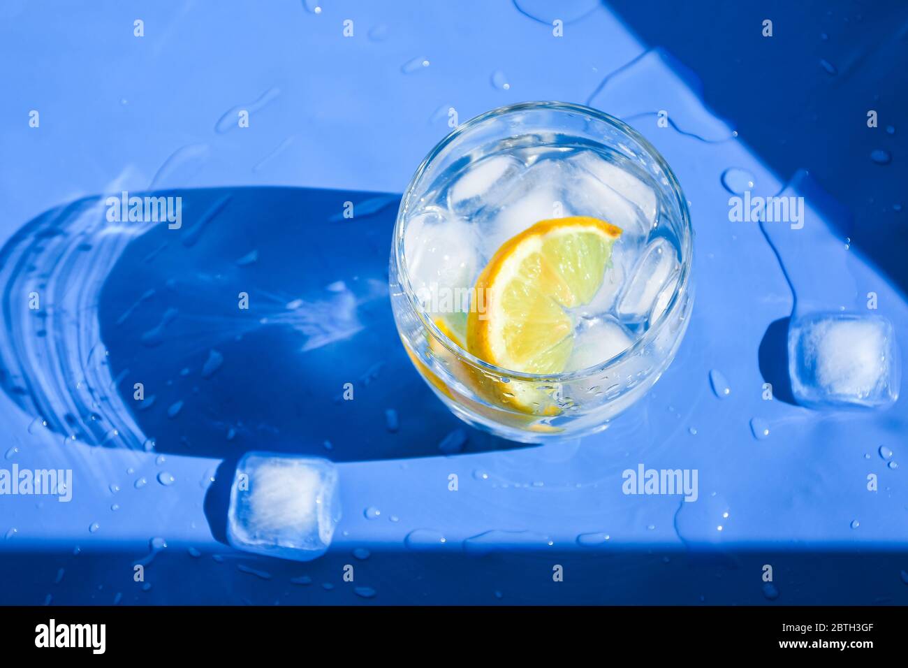 A glass of refreshing water with ice and lemon on a blue background. Heat concept, fresh. Natural light. Flat lay, top view, copy space Stock Photo