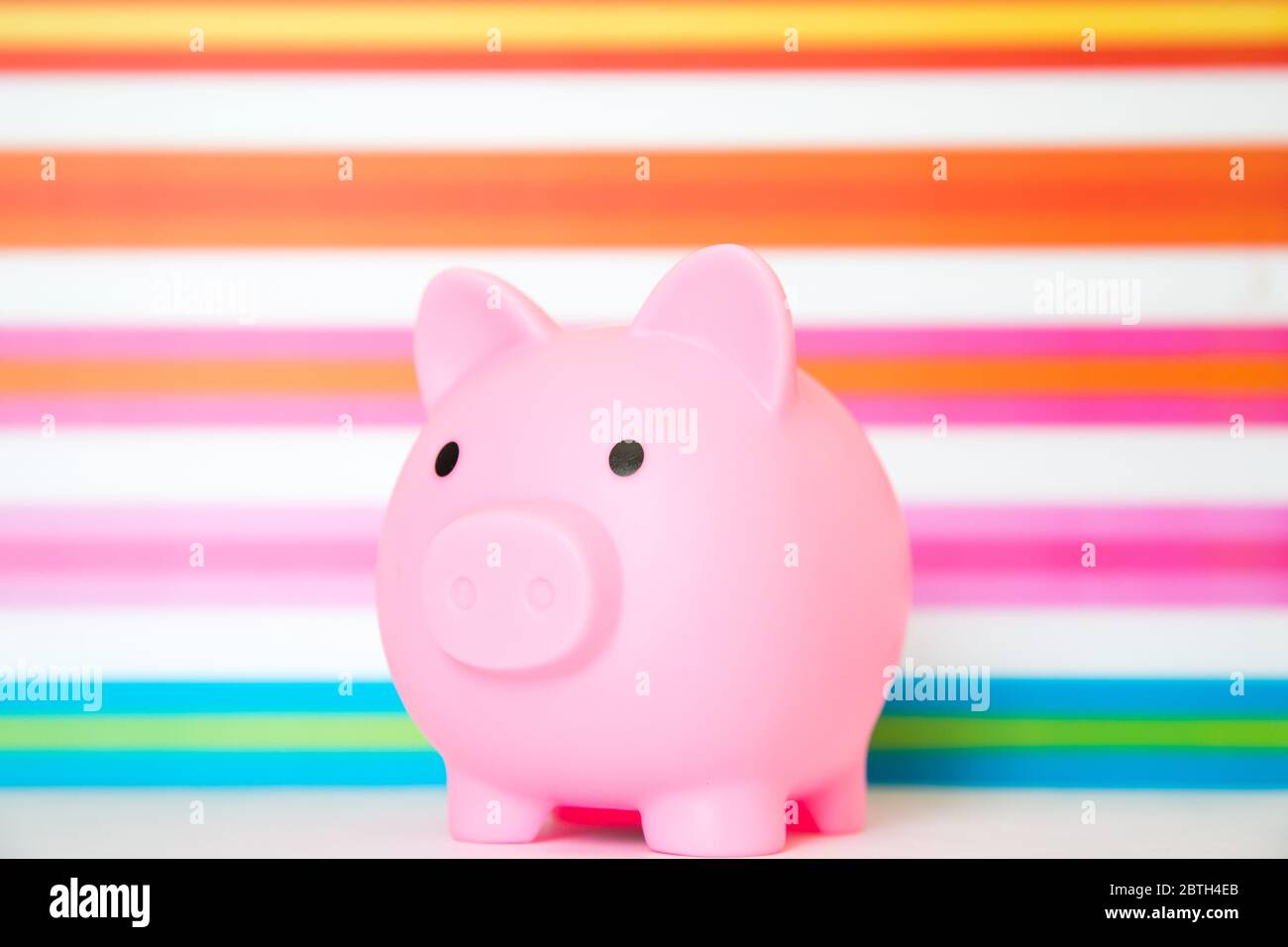 A pink, children's Piggy Bank to encourage kids to save their allowance and pocket money on a colourful, rainbow background Stock Photo