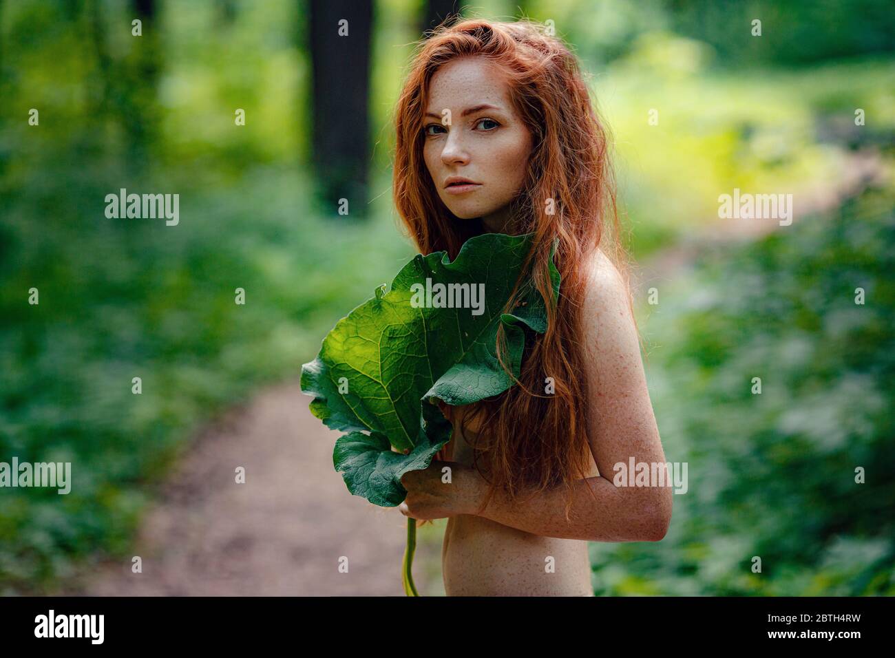 Protection of the environment, rescue of plants and nature. A young ginger woman stand in the green fairy forest. Idea and concept of Arbor day or Mot Stock Photo
