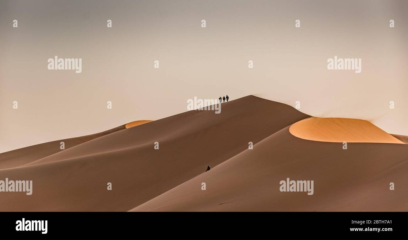Three people standing ontop of sand dunes Stock Photo