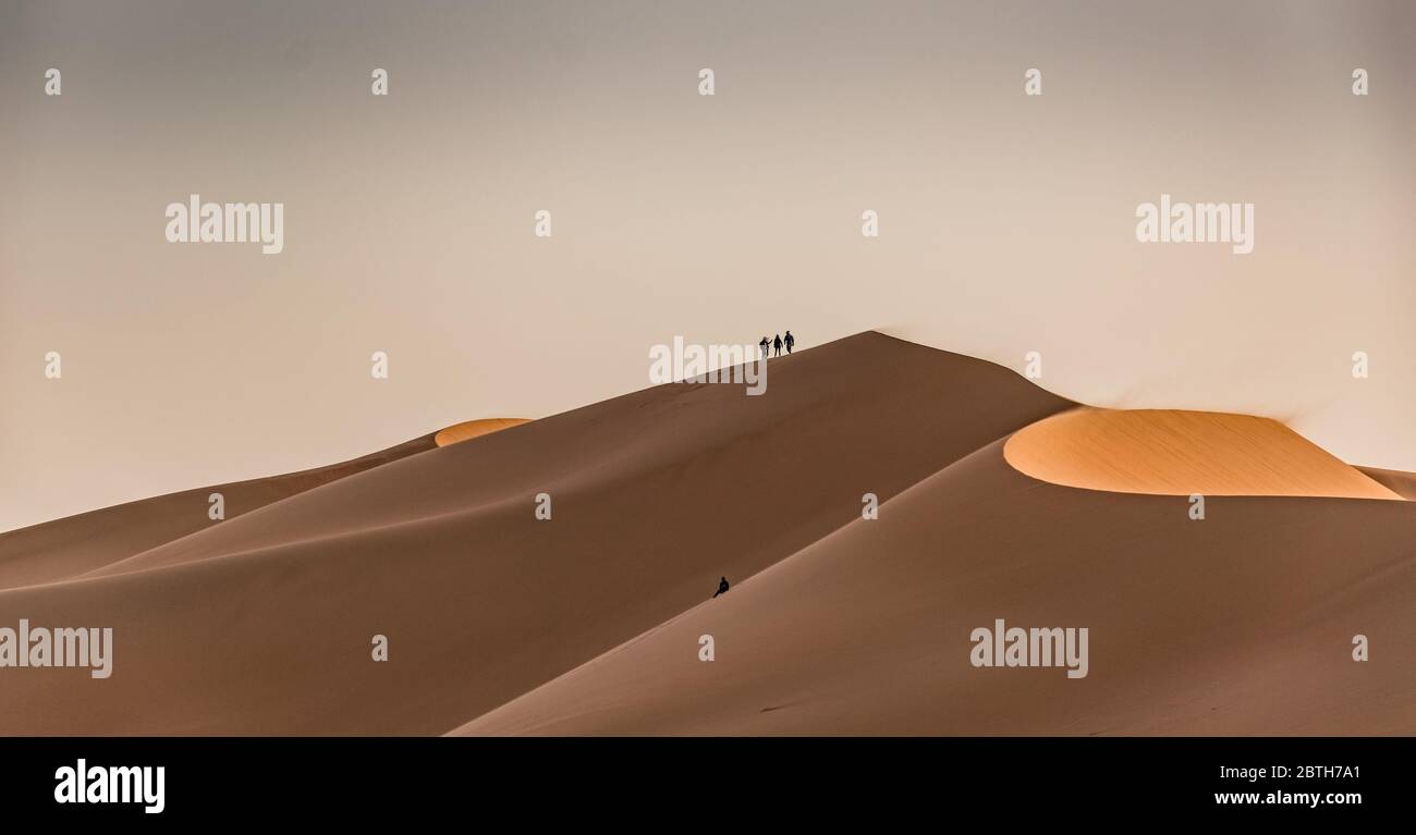 Three people standing ontop of sand dunes Stock Photo - Alamy
