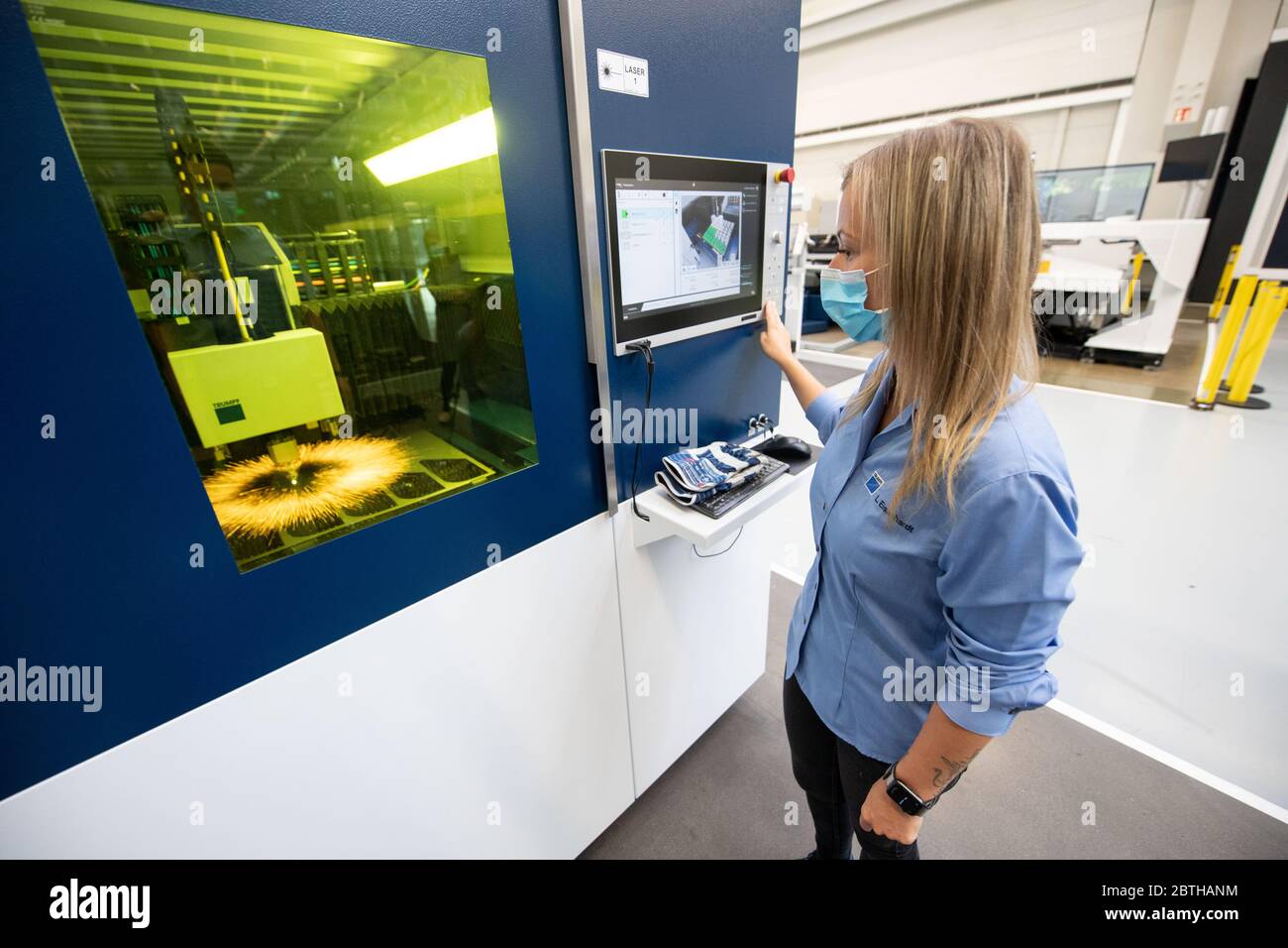 Ditzingen, Germany. 26th May, 2020. An employee of the machine manufacturer  Trumpf operates a laser cutting machine in the company's demonstration  centre. She wears a mask over her mouth and nose. (To