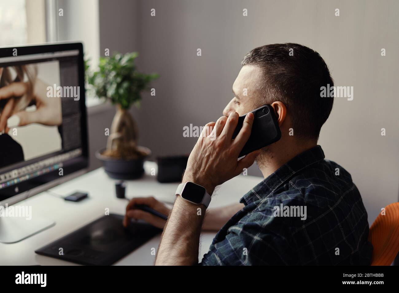 Designer in casual wear working on computer and having phone call while looking at the monitor Stock Photo