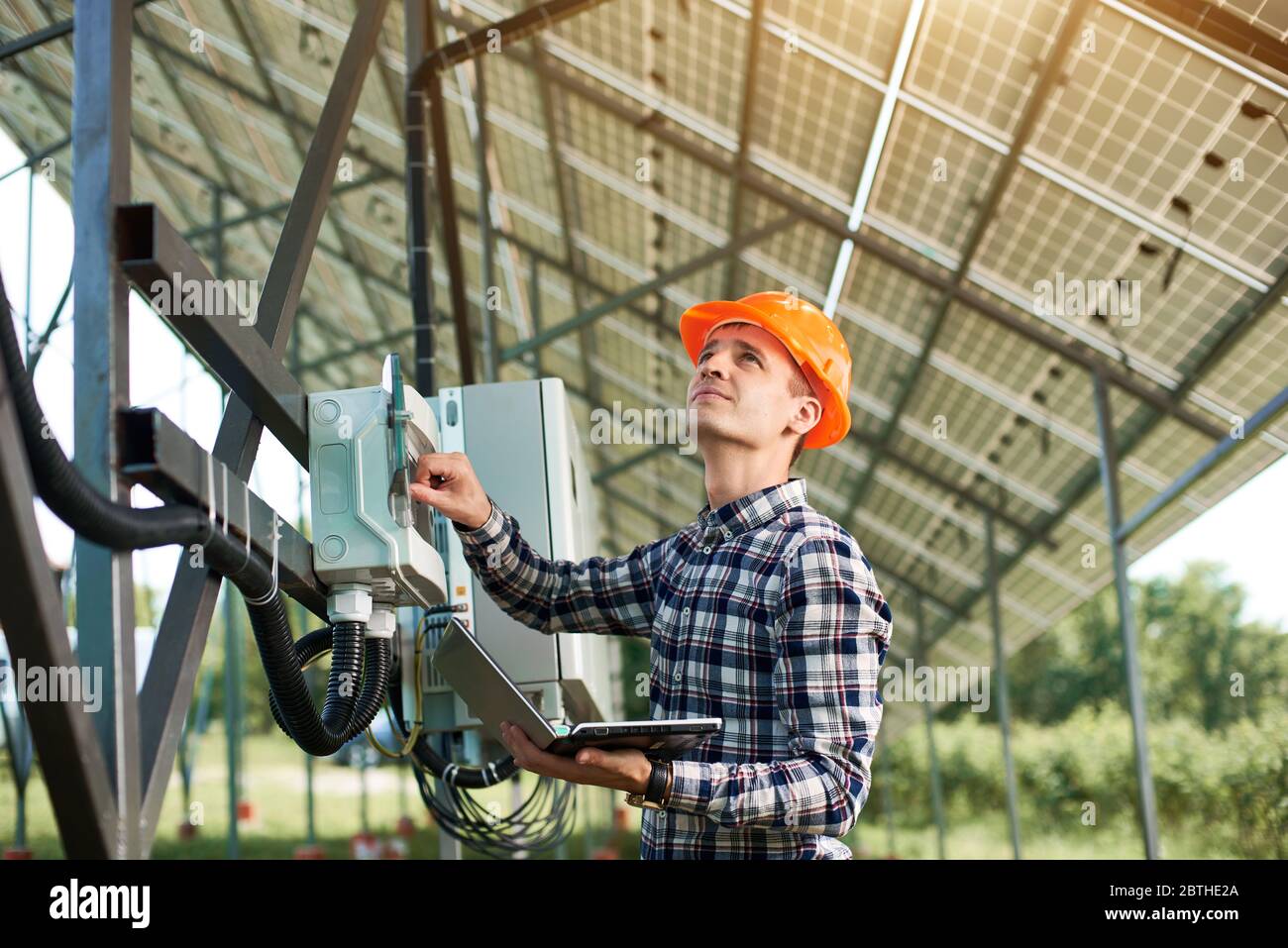 Male engineer in helmet and with laptop pushing button at the ...