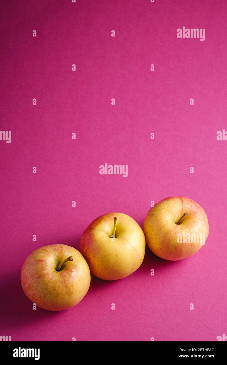 Fresh sweet three apples on pink purple textured background, angle view copy space Stock Photo