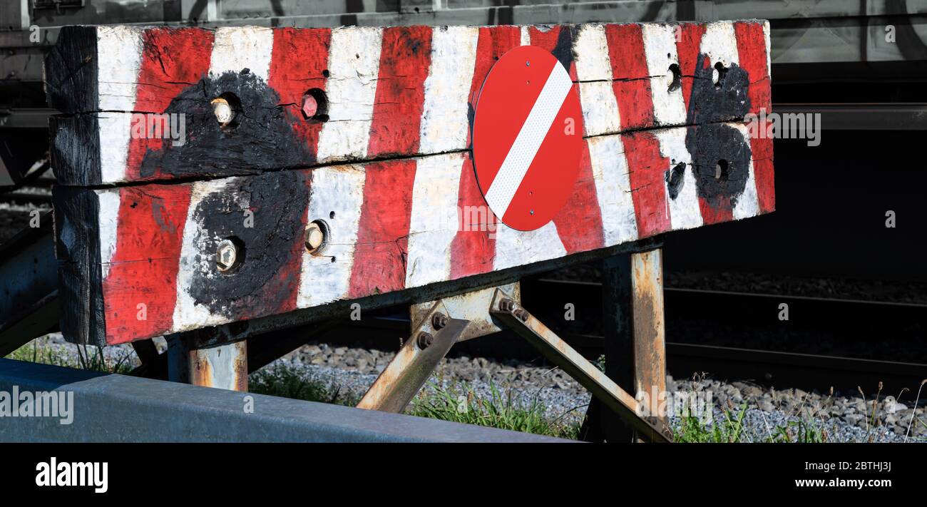 railway buffer stop with heavily worn wood in red-white painted stripes with red-white stop sign during the day Stock Photo