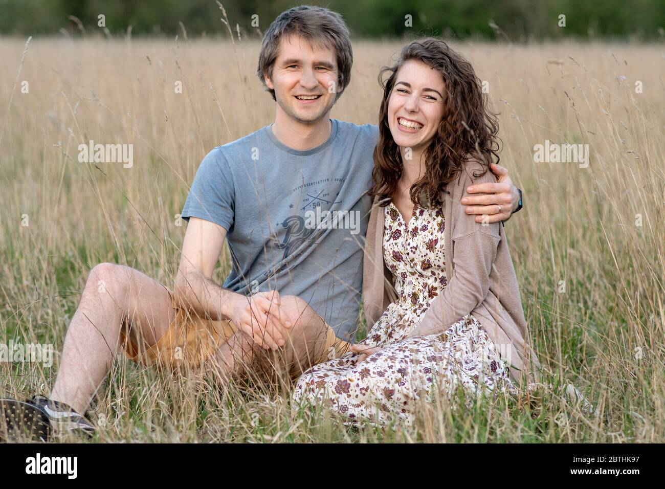 A young attractive beautiful couple smile together in a beautiful outdoor field showing their love for each other and kissing Stock Photo