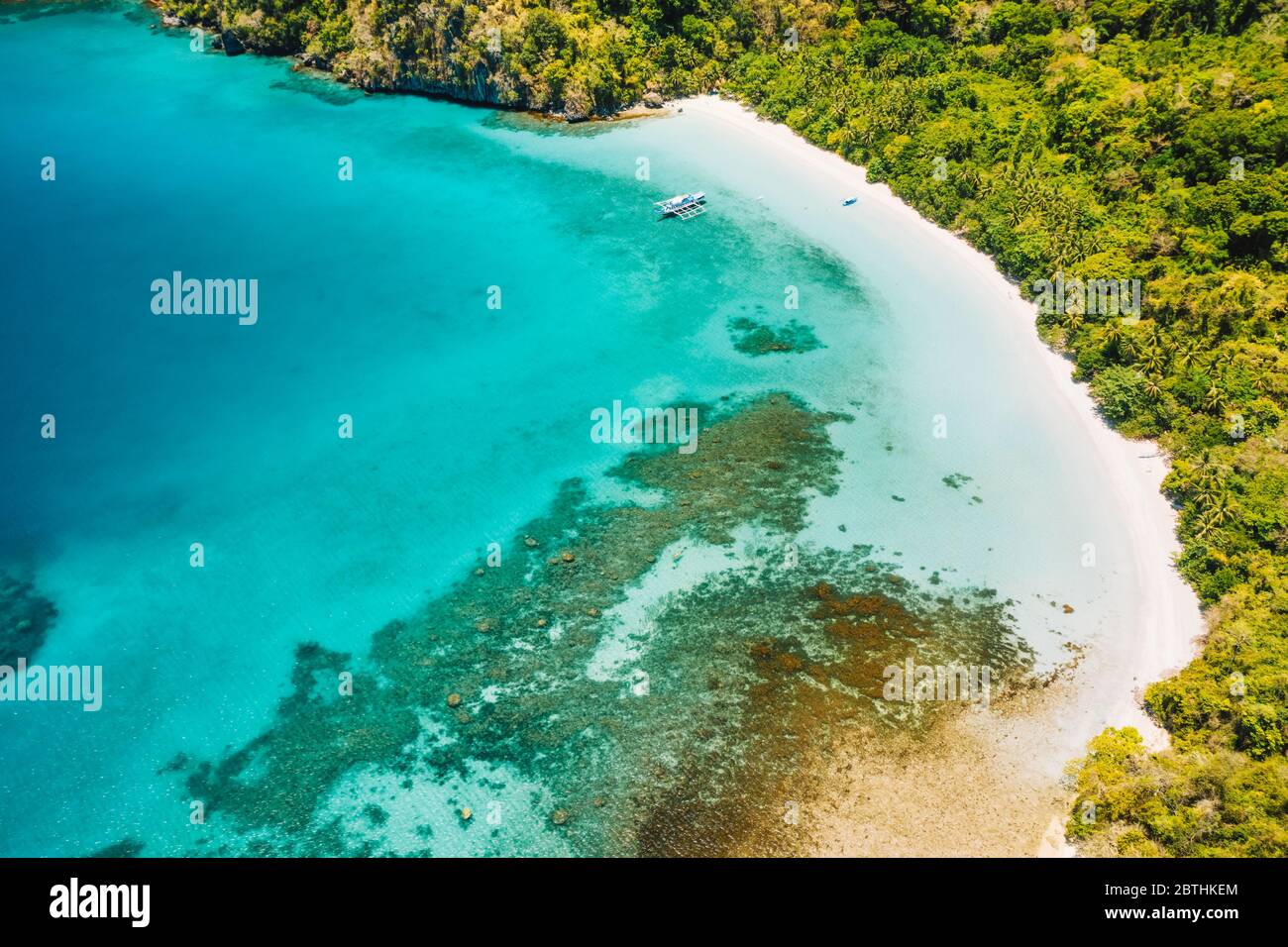 Aerial drone view of lonely boat at beautiful deserted tropical beach and blue lagoon surrounded by lush green jungle. Cadlao Island, El Nido, Palawan Stock Photo