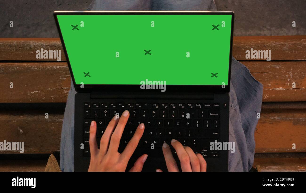 Woman typing on a laptop sitting on a bench. Stock Photo