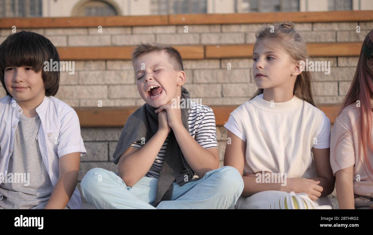 Four kids looking bored and overtired seating on a bench. Stock Photo