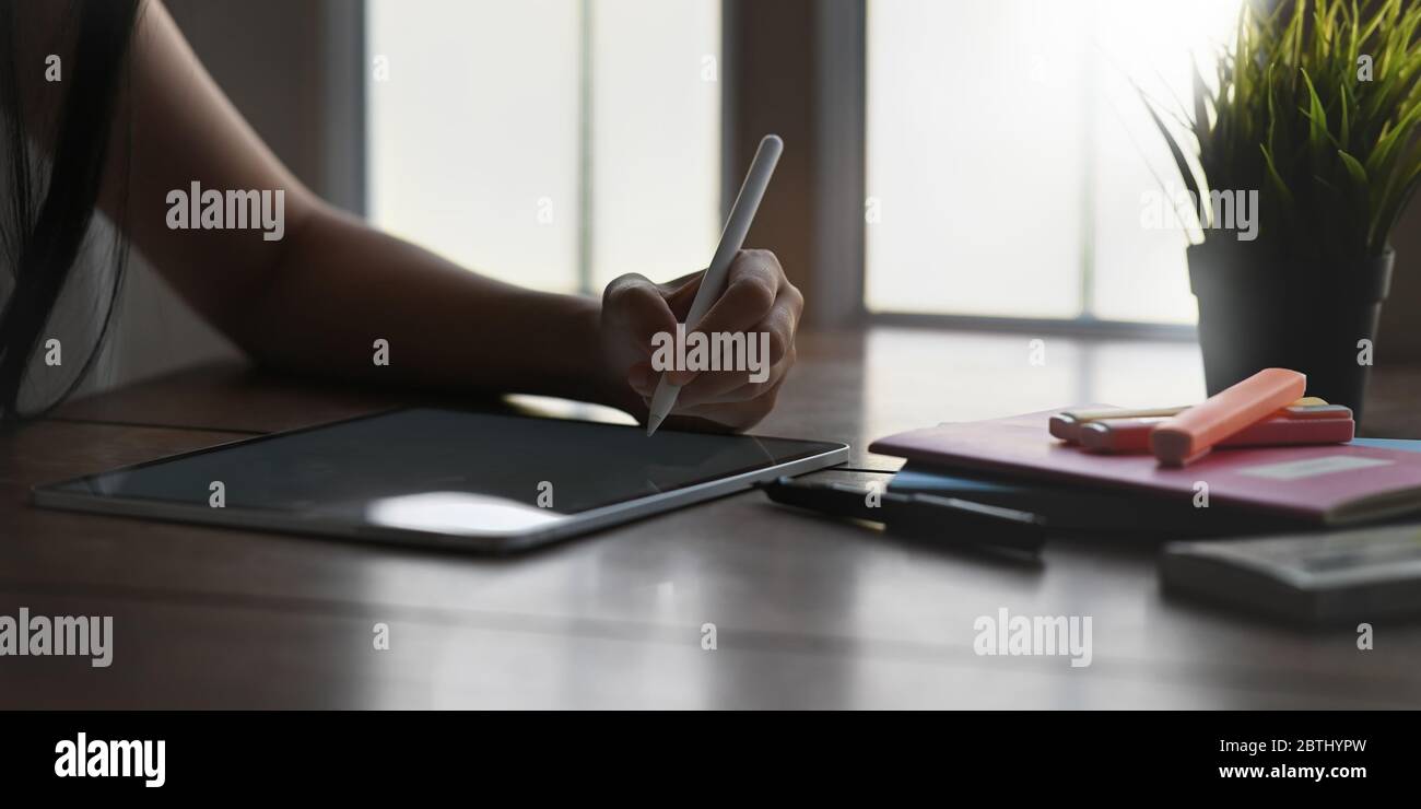 Cropped of beautiful woman sketching on computer tablet by using a stylus pen and sitting at the wooden working desk over comfortable living room wind Stock Photo