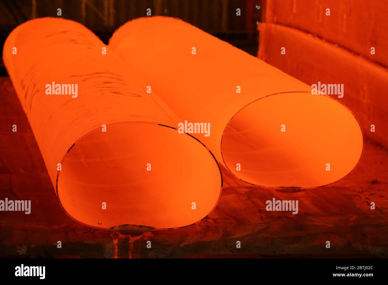 Large red hot steel tubes coming out of the rolling and forming mill Stock Photo