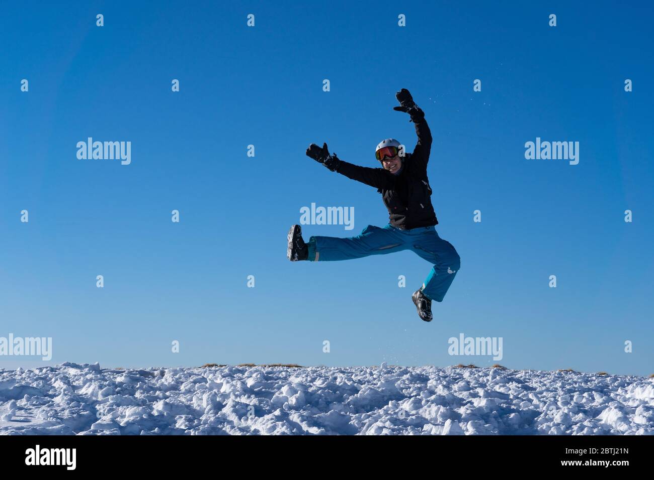 Girl with goggles and helmet is leaping midair in winter. Blue sky and bright sunshine on the top of mountains in Switzerland. Concept. Stock Photo