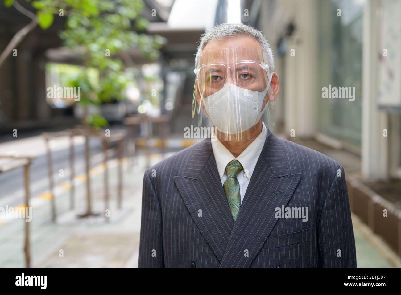 Mature Japanese businessman with mask and face shield in the city Stock Photo