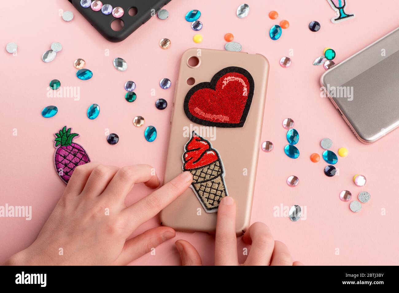 Girl putting red heart and ice cream patches onto beige phone case Stock Photo