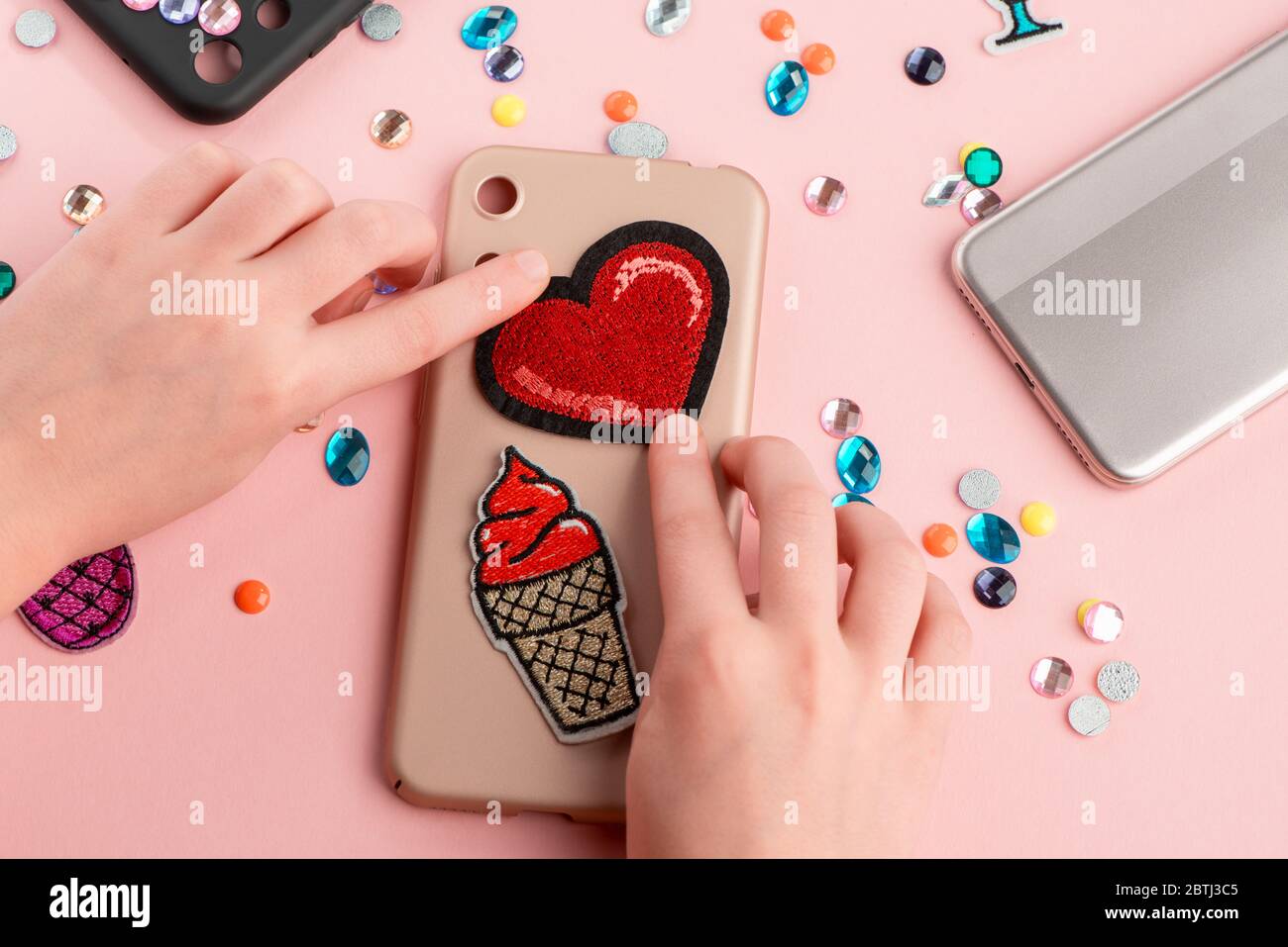 Girl putting red heart and ice cream patches onto beige phone case Stock Photo