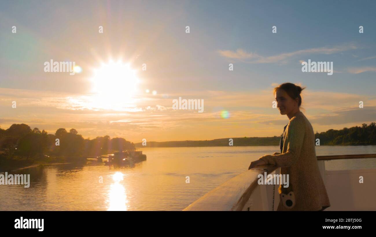 Woman standing on deck of cruise ship and looking at landscape. Sunset ...