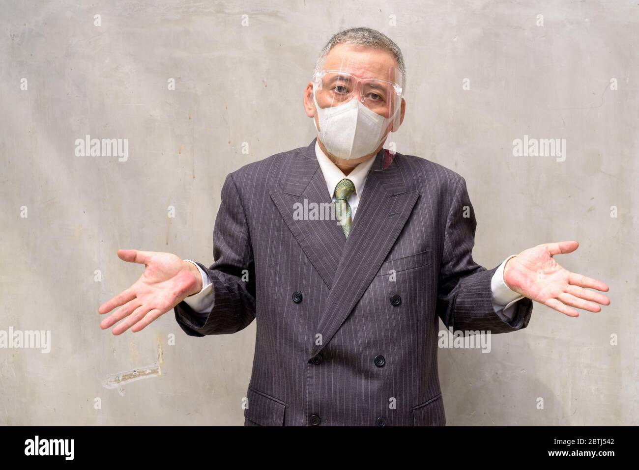 Mature Japanese businessman with mask and face shield shrugging shoulders Stock Photo