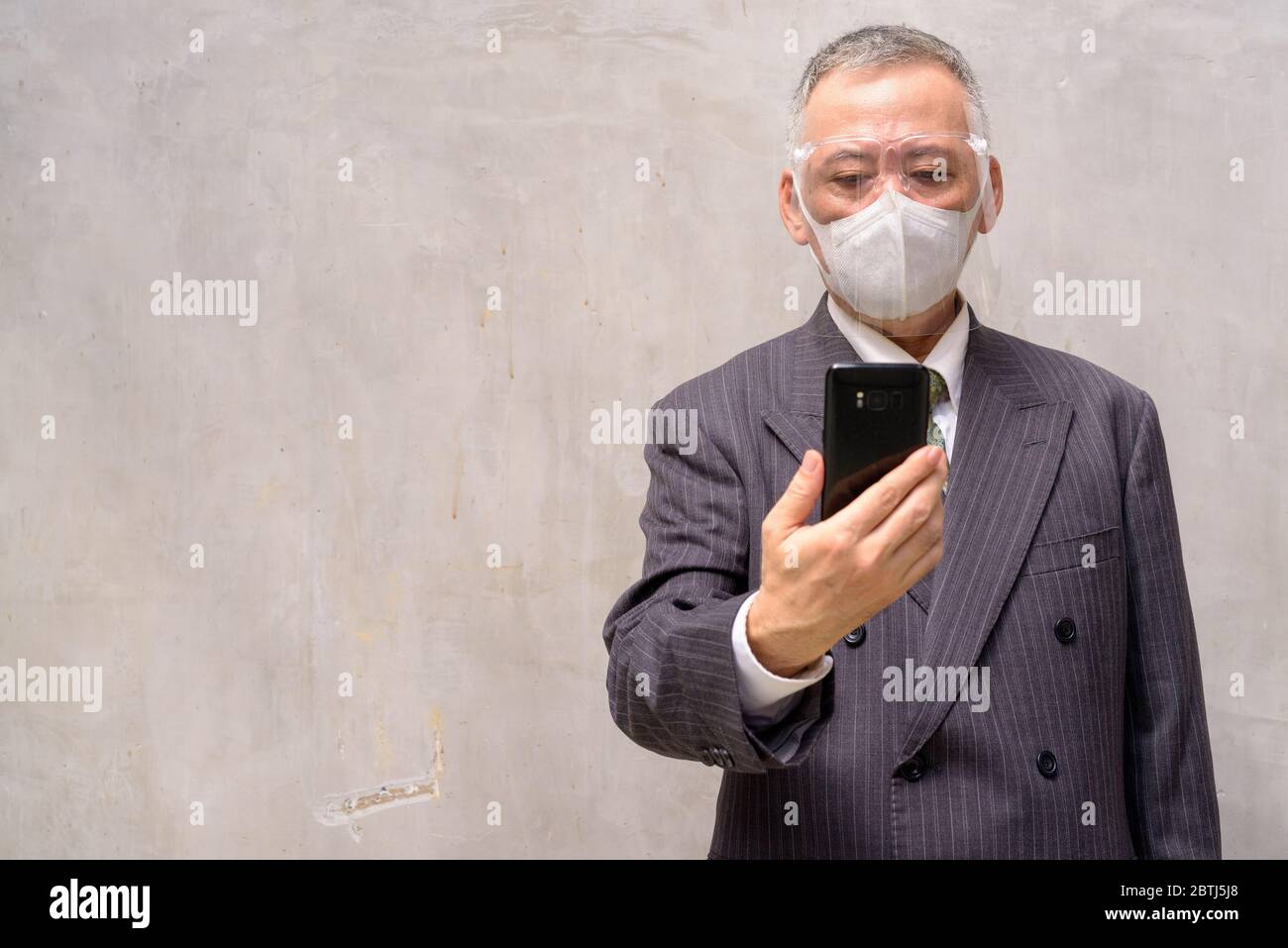 Mature Japanese businessman with mask and face shield using phone Stock Photo