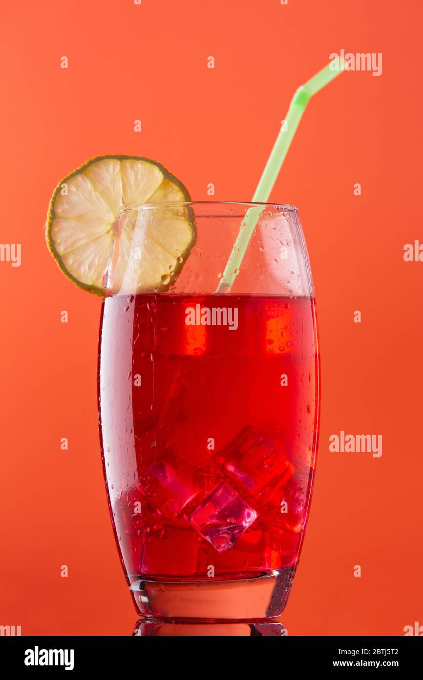 glass of cold red drink on an orange background in a nice glass and with a straw ready to drink Stock Photo