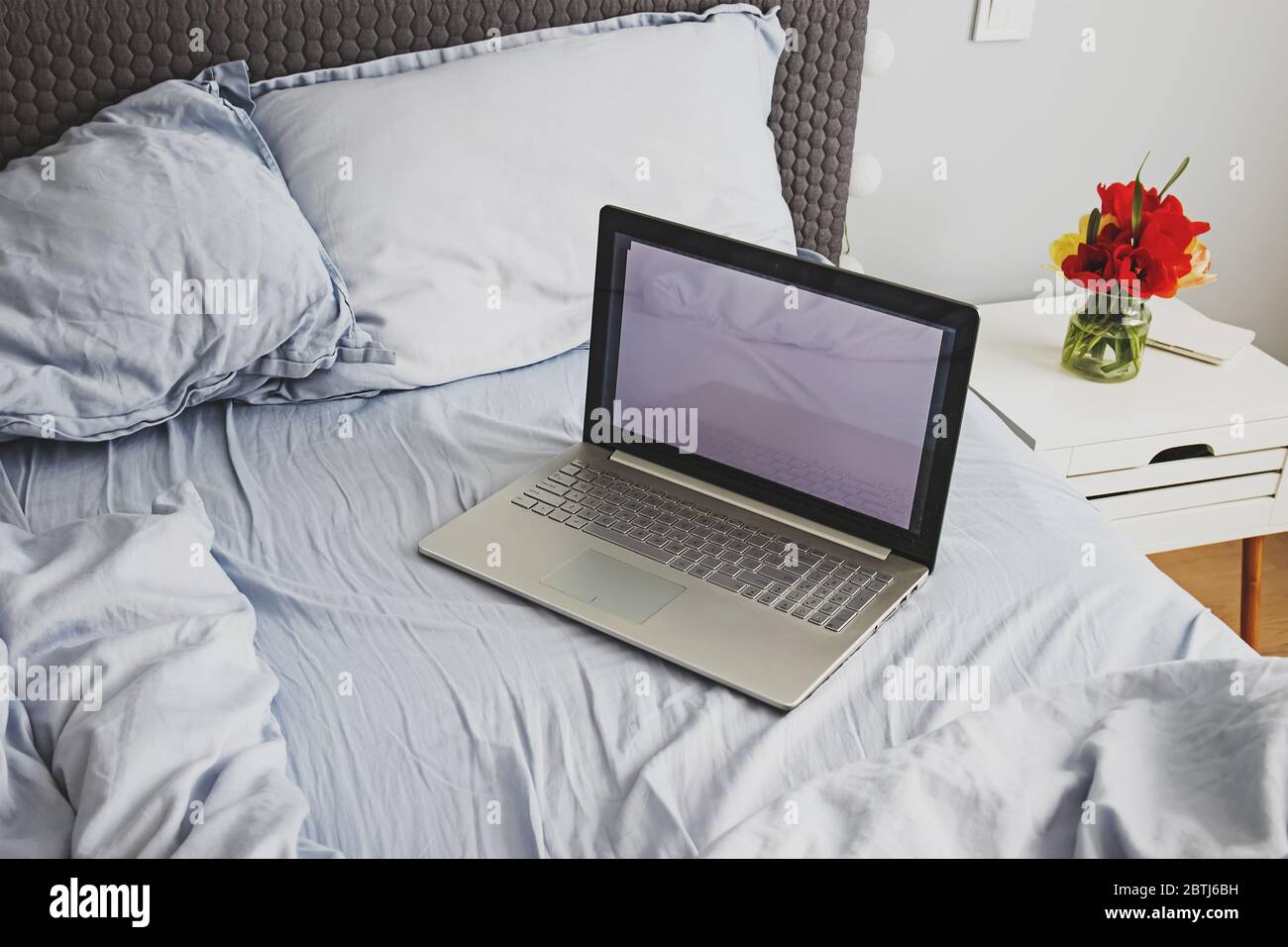 Empty messy grey bed with laptop in minimalist bedroom Stock Photo Alamy