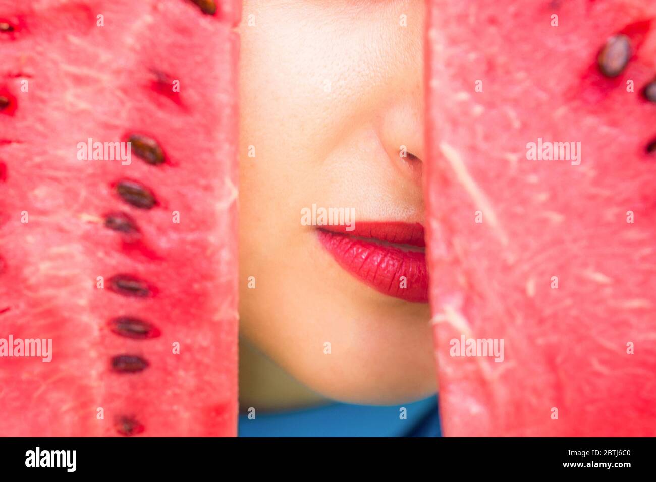 Close Up Of Young Woman Covering Her Face Between Two Pieces Of Watermelon Peeking Lips With Red 