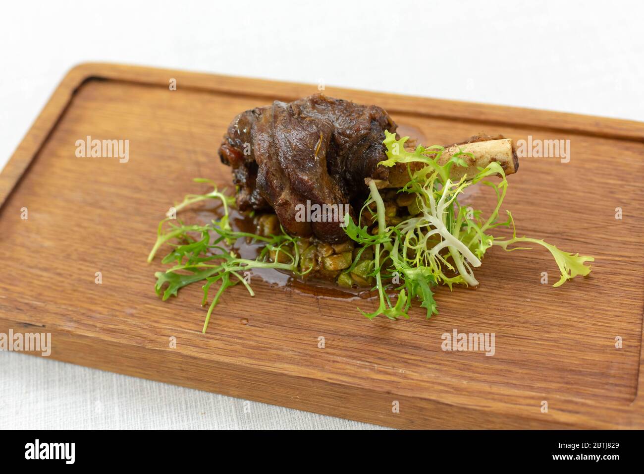 roasted meatshank baked whole lies with fresh tomato greens and hot pepper on a platter on an old wooden surface Stock Photo