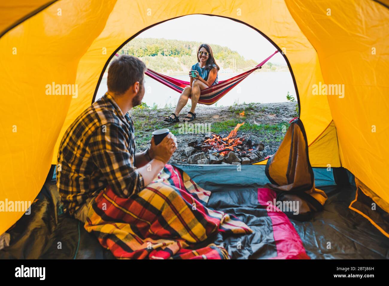 couple resting near fire. man sitting in tent woman laying on hammock Stock Photo