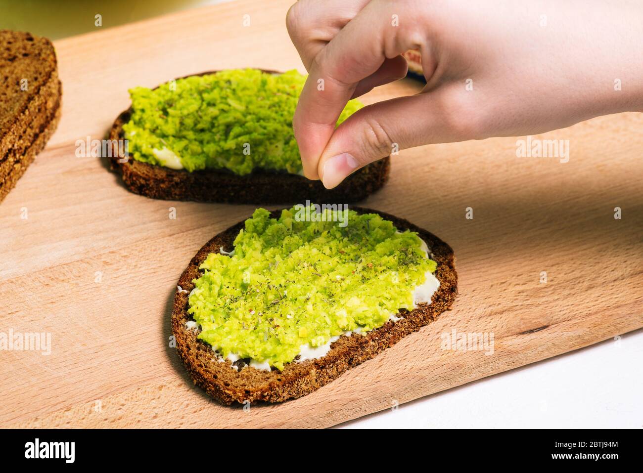 The cook sprinkles spices on a ready-made avocado sandwich. Healthy food for Breakfast, lunch or dinner. Vegetarian recipe Stock Photo