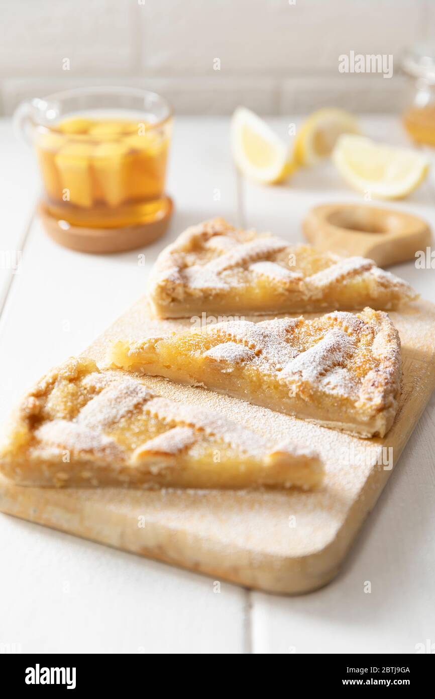 Three pieces of homemade shortbread lemon pie sprinkled with powdered sugar on a cutting board. Tea in a mug and lemon slices in the background. Stock Photo