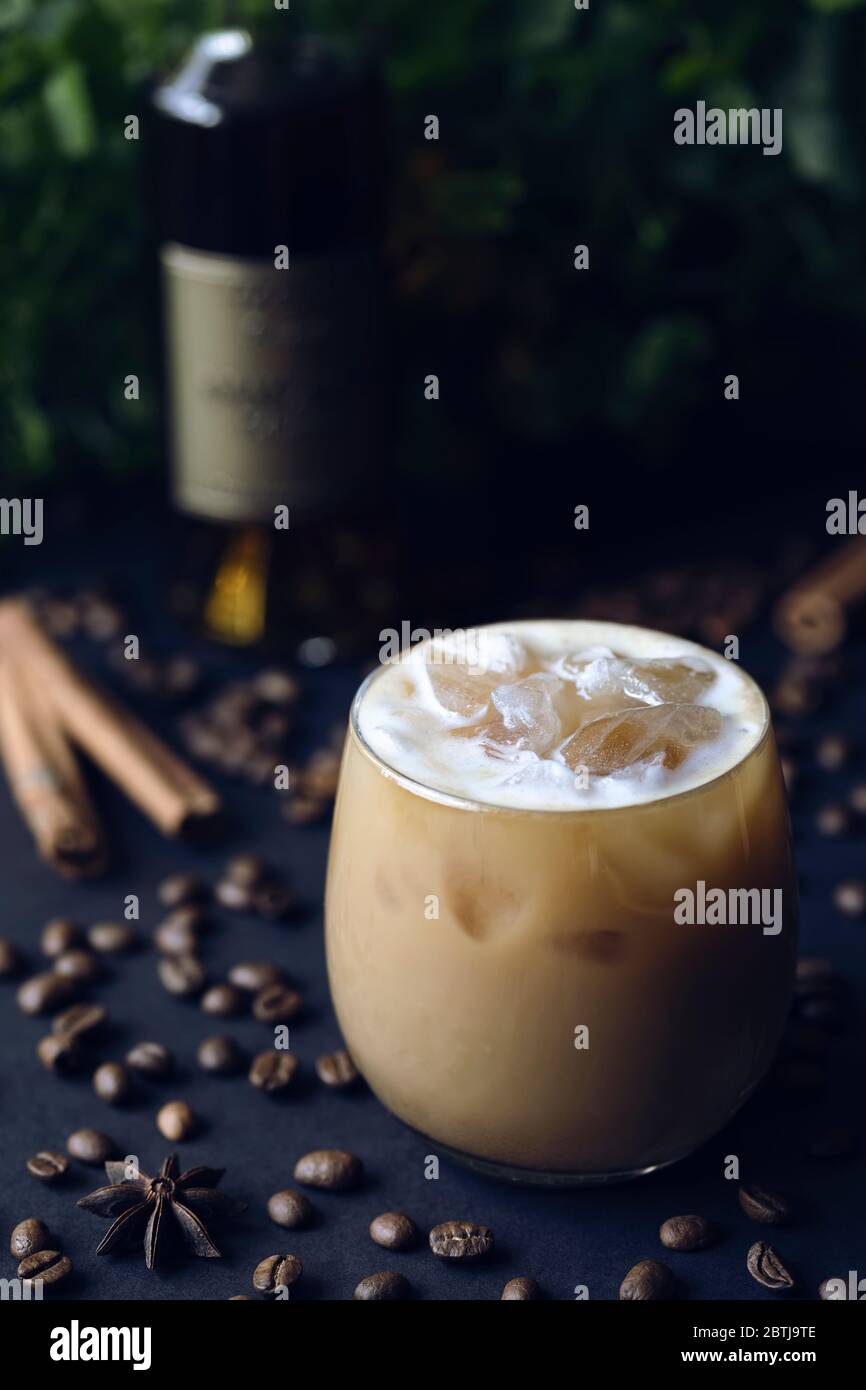 Cold spicy coffee cocktail with ice on dark background with cognac bottle, coffee beans, anise star and cinnamon sticks Stock Photo