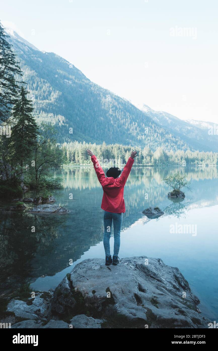Woman hiker raising her hands up in the air. People success, victory and power. Back view of a girl standing on a rock looking at mountain view. Hiker Stock Photo