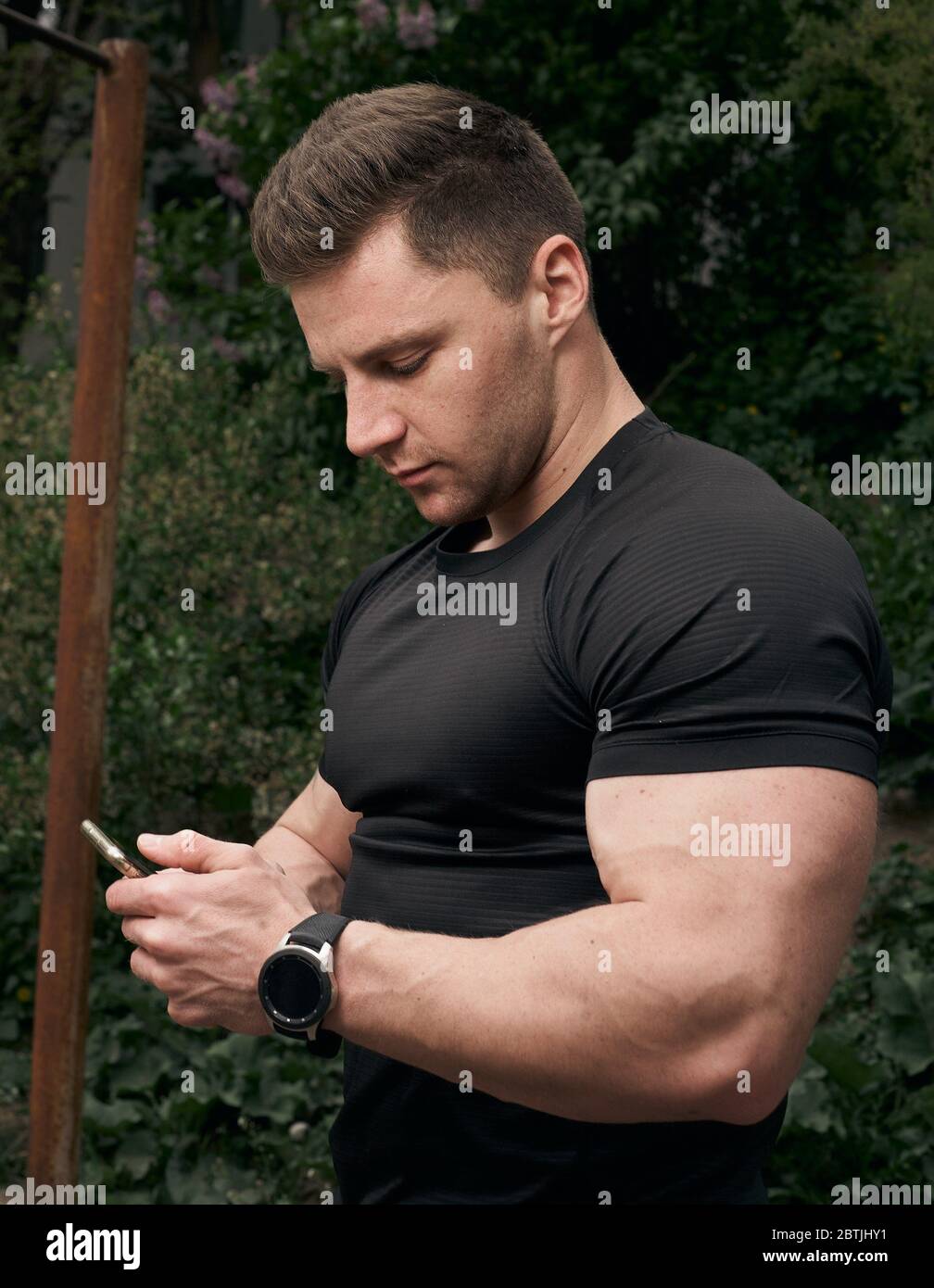 The guy uses a smartphone for training. Athletic guy is training outdoors. Concept mobile application for training. Stock Photo