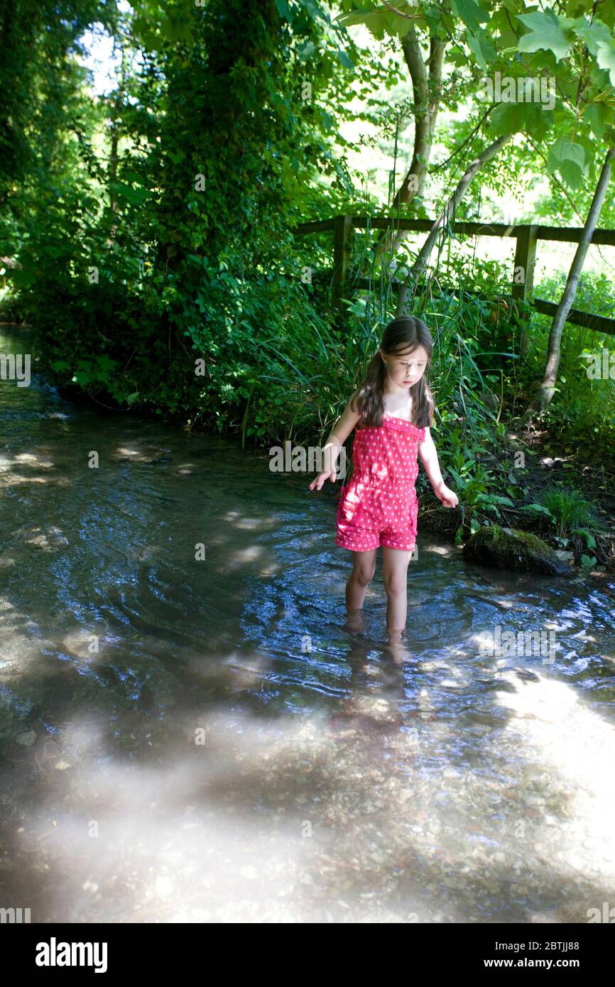 Young girl in red dress paddling in stream Stock Photo