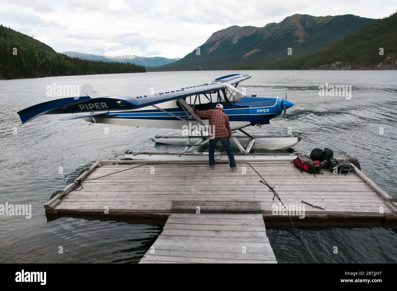 A single-engine, two-seater Piper Cub floatplane and pilot, on a lake in Spatsizi Plateau Wilderness Provincial Park, in British Columbia, Canada. Stock Photo