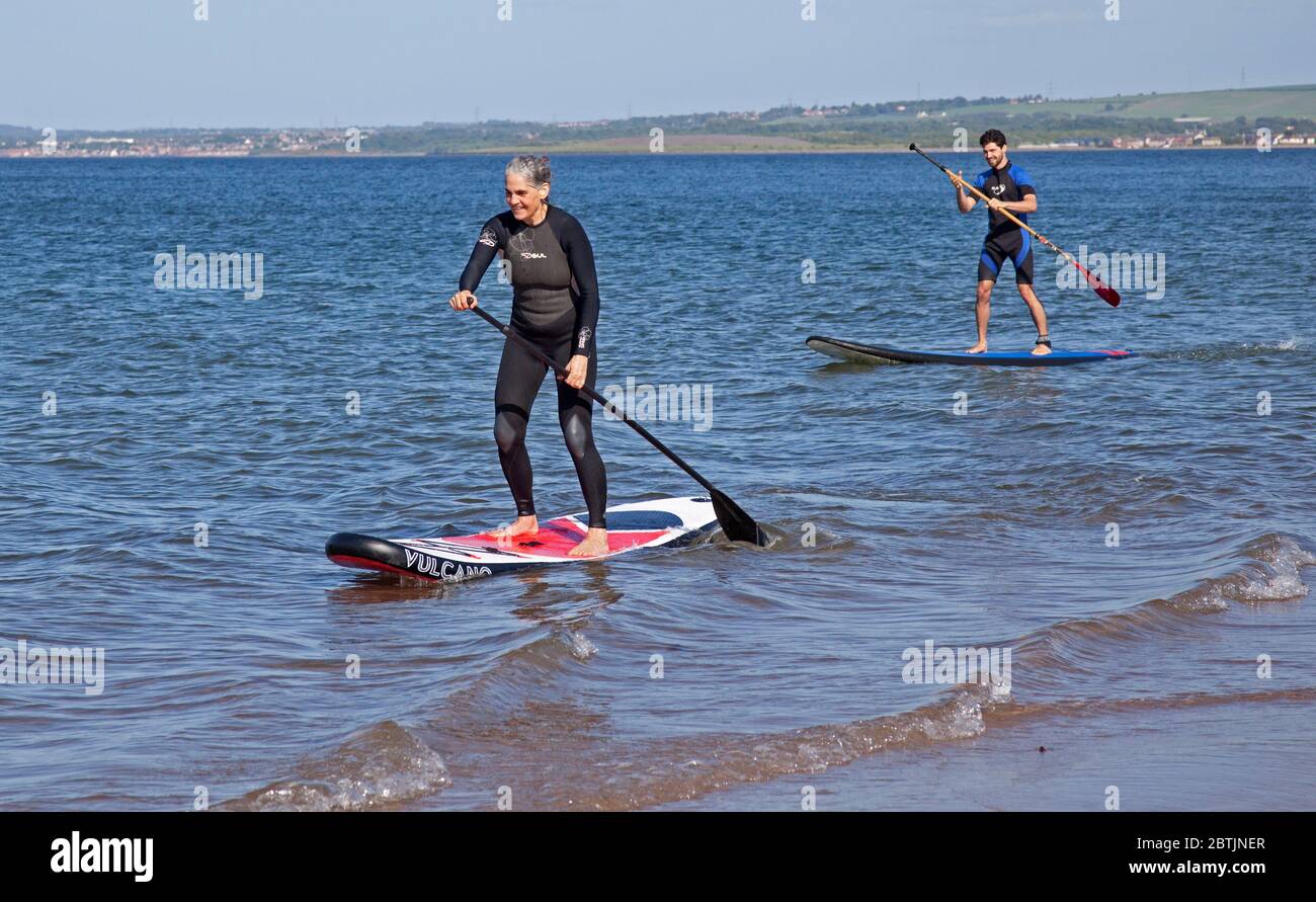 Portobello, Edinburgh, Scotland, UK. 26 May 2020. More relaxed atmosphere at the seaside late afternoon as Scotland nears the end of Phase 1 of Coronavirus Lockdown. Temperature of 19 degrees and sunny. Pictured the Harrison family, mum and her sons enjoy stand up paddle boarding. Stock Photo