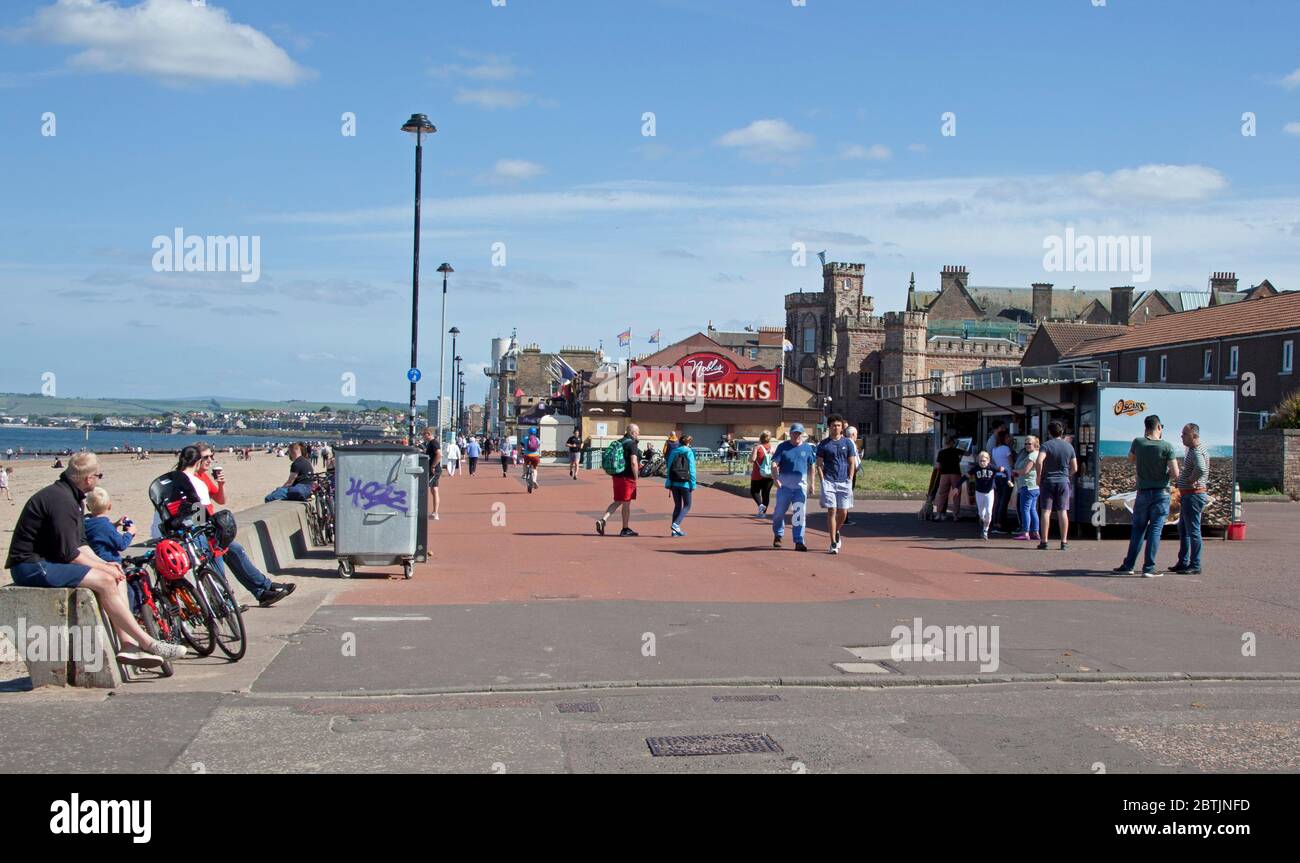 Portobello, Edinburgh, Scotland, UK. 26 May 2020. More relaxed atmosphere at the seaside late afternoon as Scotland nears the end of Phase 1 of Coronavirus Lockdown. Temperature of 19 degrees and sunny. People relax on the promenade and queue at the snacks van. Stock Photo