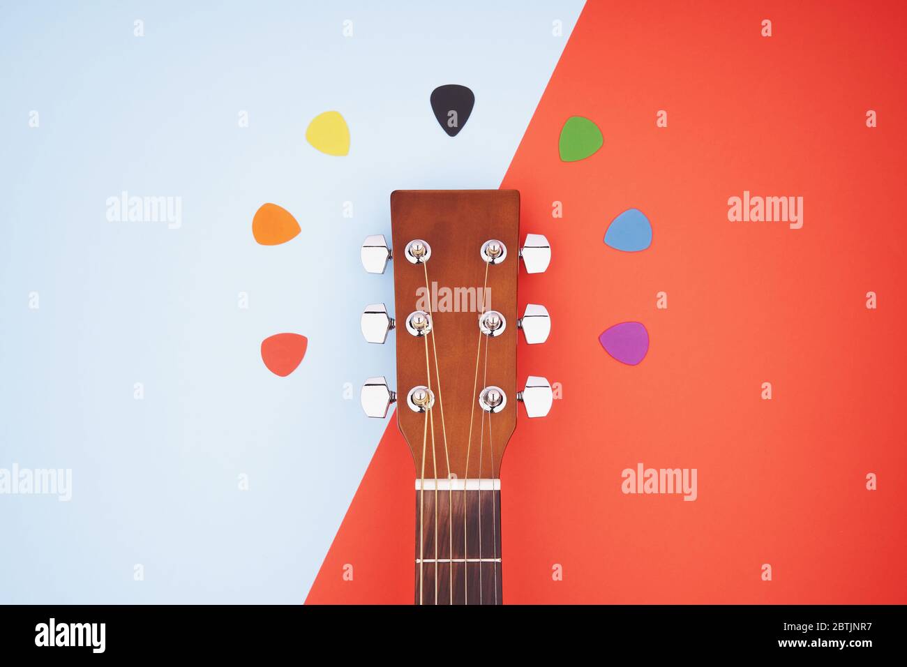 Colorful picks around acoustic guitars headstock. Flat lay on light blue and red background Stock Photo
