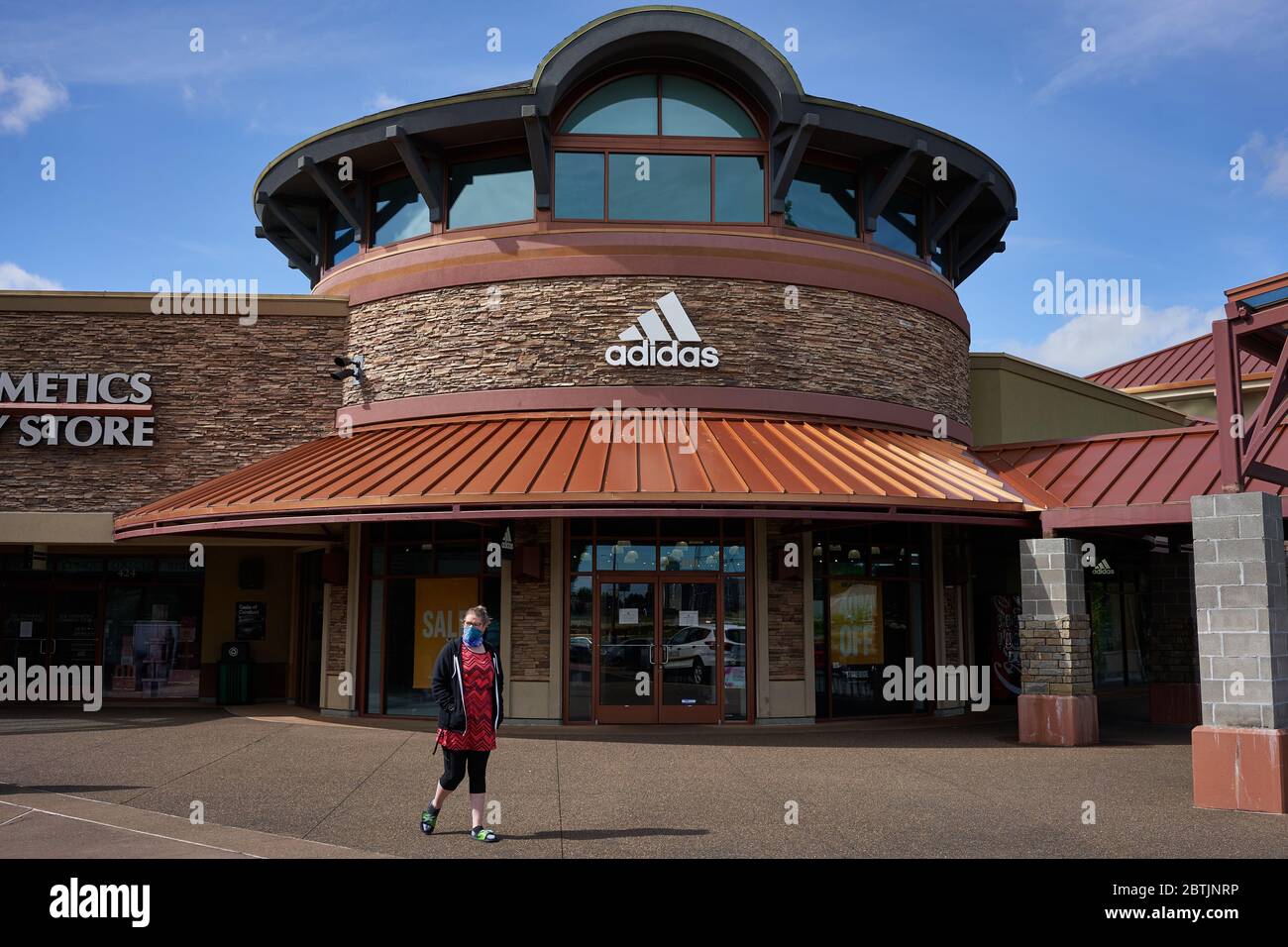 A face-covered shopper passes a closed Adidas store in the reopened Woodburn Premium Outlets Oregon on Memorial Day weekend during COVID-19 crisis Stock