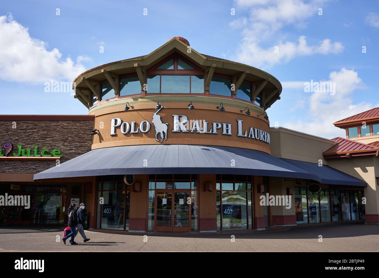 Masked shoppers walk past a closed Polo Ralph Lauren store in Woodburn Premium Outlets in Oregon on Memorial Day during the coronavirus pandemic. Stock Photo
