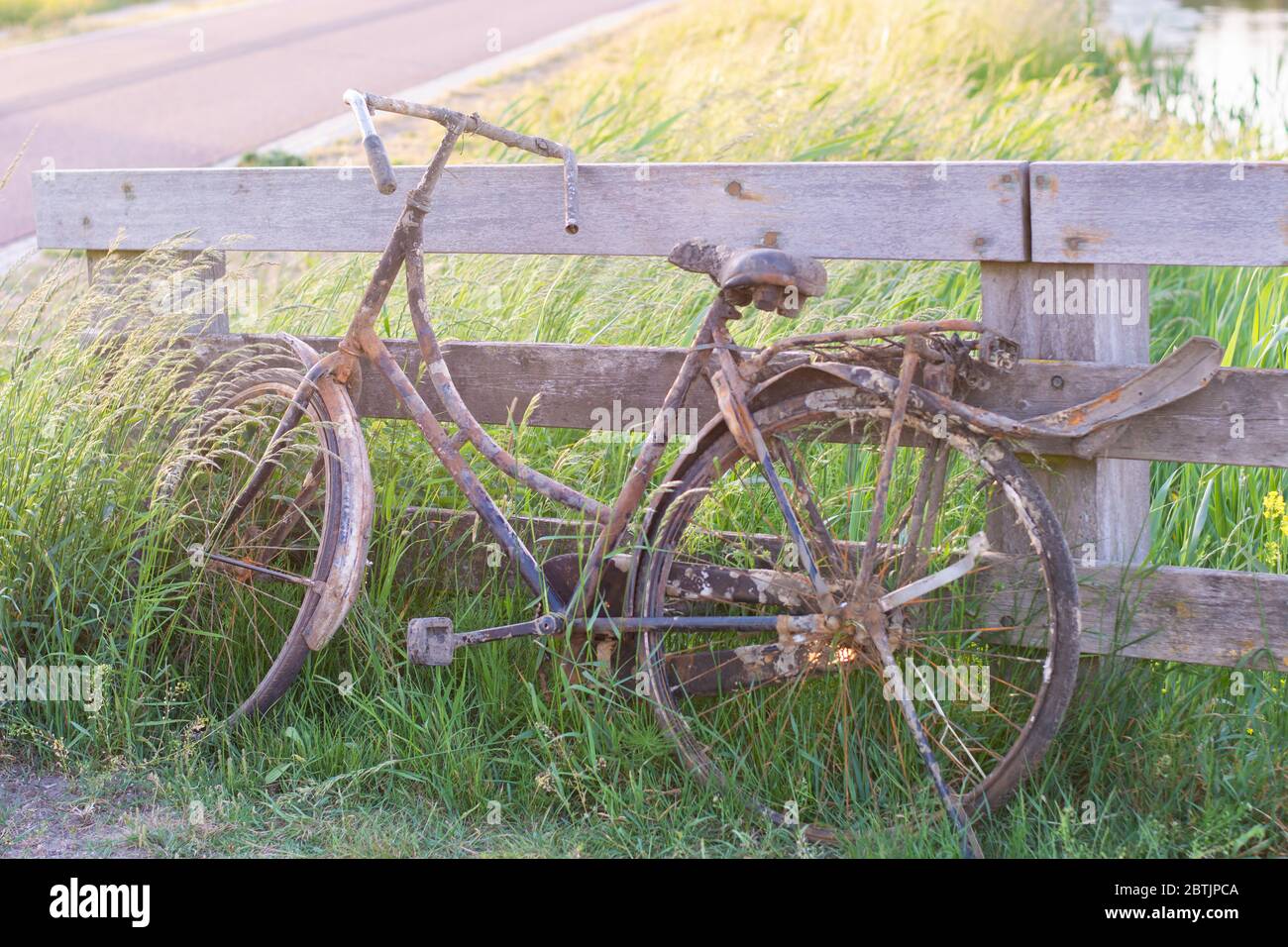 An old abandoned rusty bike parked against wooden fence. Old fashioned classic bicycle stands forgotten along a bicycle path. Fished out of the ditch Stock Photo
