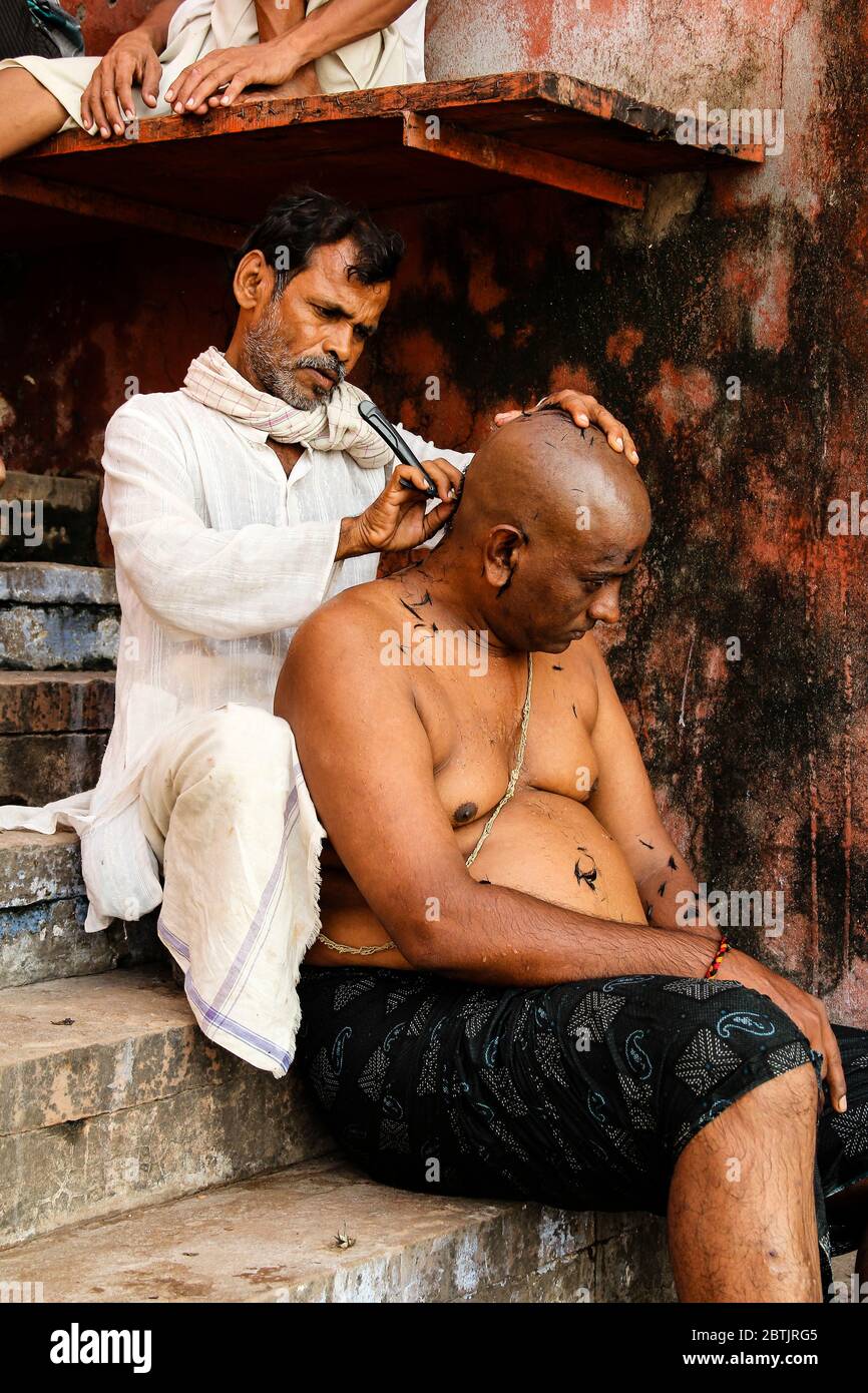 India, Varanasi - Uttar Pradesh state, 31st July 2013. On a staircase in front of the Ganges river, a barber shaves a client. Stock Photo