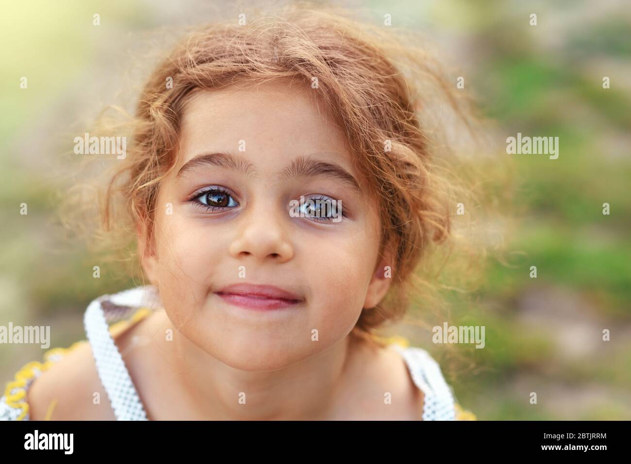Portrait of smiling cute little girl at green of summer park. Happy child looking at the camera Stock Photo