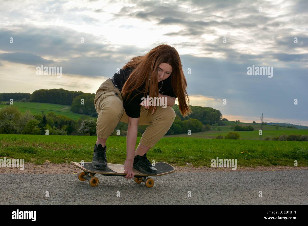 A young girl squats skateboarding on a road in green nature Stock Photo -  Alamy