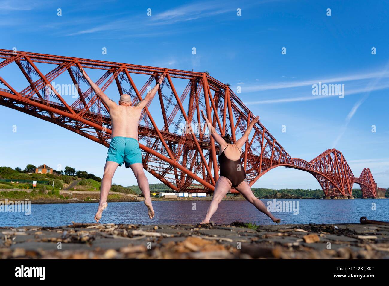 North Queensferry, Scotland, UK. 26 May 2020. Kenny McAlpine and Jenny Waring from Fife Wild Swimmers group make the most of the warm sunshine and an exercise escape from the Covid-19 lockdown and jump into the Firth of Forth at North Queensferry with the Forth Bridge as a dramatic backdrop. Iain Masterton/Alamy Live News Stock Photo