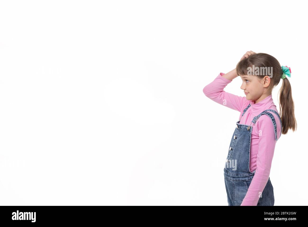 The girl puzzled scratches her head and looks at an empty spot in the frame. Stock Photo